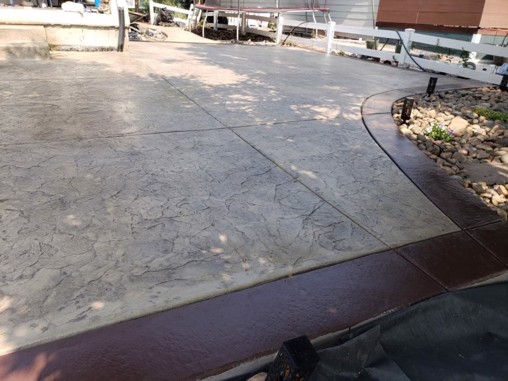 Stamped concrete patio in Loveland, CO, with a textured stone finish and a curved border next to a landscaped rock garden