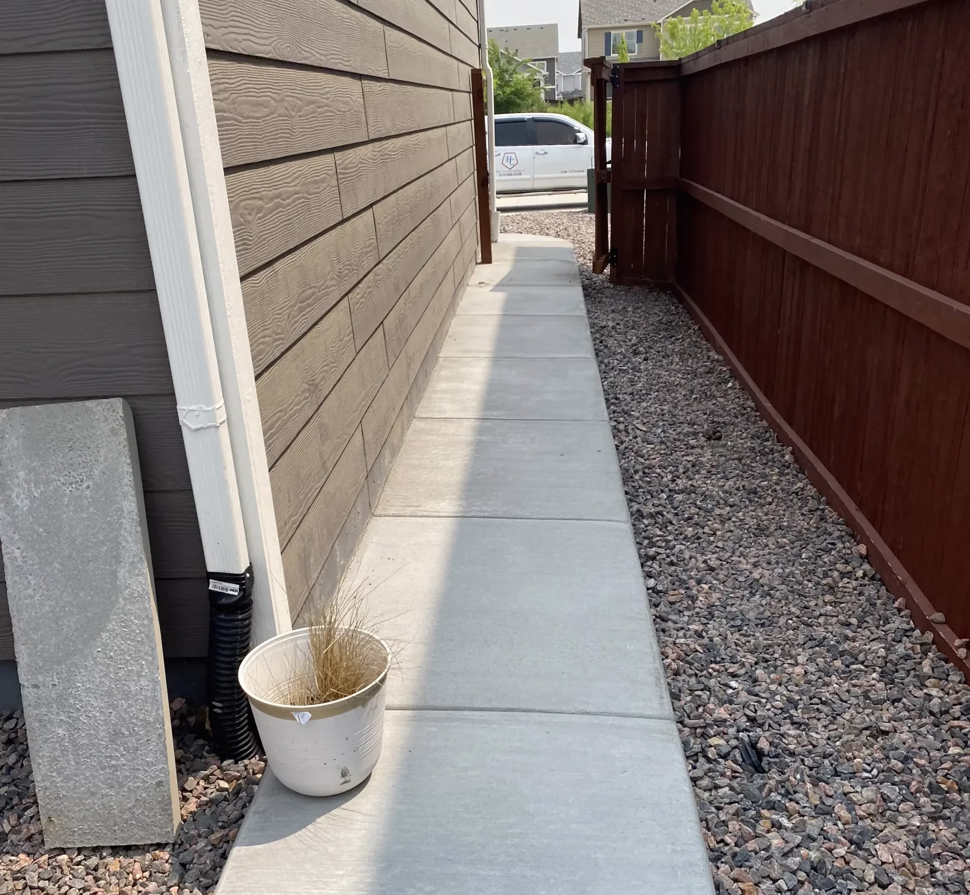 A smooth concrete walkway beside a house in Loveland, CO, with a wooden fence and gravel