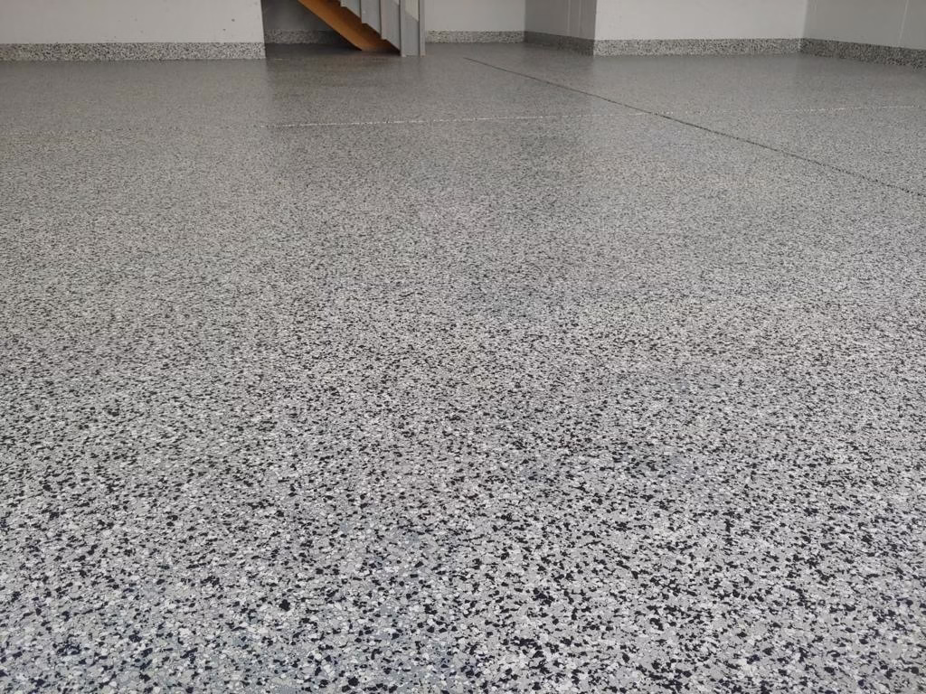 Epoxy flake garage flooring installation in Longmont, Colorado by Hugo's Concrete, featuring decorative flakes with protective blue tape edges