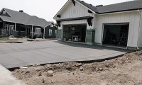 A concrete driveway in the process of completion in front of a modern home in Colorado, illustrating a fresh, smooth concrete installation. The image captures a typical scene during driveway construction, highlighting considerations for either repairing or replacing concrete driveways, showing the prepared ground and newly laid sections that blend into the existing home's aesthetic.