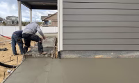 Concrete contractor in Fort Collins, CO, working on a new concrete patio installation beside a grey house.