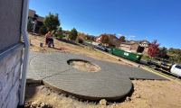 Workers pouring and shaping stamped concrete for a driveway in a residential area of Northern Colorado, showcasing skilled concrete pouring techniques under clear skies.
