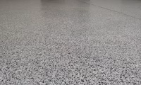 Epoxy flake garage flooring installation in Longmont, Colorado by Hugo's Concrete, featuring decorative flakes with protective blue tape edges