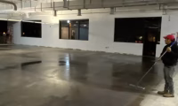 Worker applying sealant on a freshly laid concrete floor in an industrial building, demonstrating proper concrete care techniques