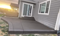 A newly installed concrete patio by a contractor at a residence in Colorado, showcasing a smooth, dark gray finish with curved edges. The setting sun casts a warm glow on the house, highlighting the durable and well-crafted outdoor living space.