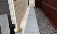 A smooth concrete walkway beside a house in Loveland, CO, with a wooden fence and gravel