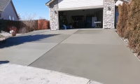 Newly installed smooth concrete driveway leading to a residential garage with stone veneer siding, showcasing professional concrete driveway installation.