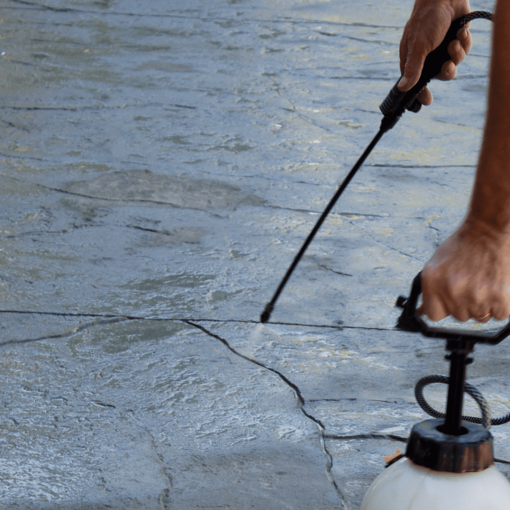 A person power washing a concrete surface using a handheld spray nozzle, demonstrating safe and effective techniques for cleaning concrete without causing damage.