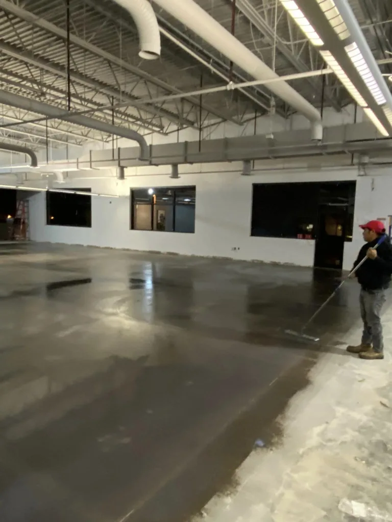 Worker applying sealant on a freshly laid concrete floor in an industrial building, demonstrating proper concrete care techniques