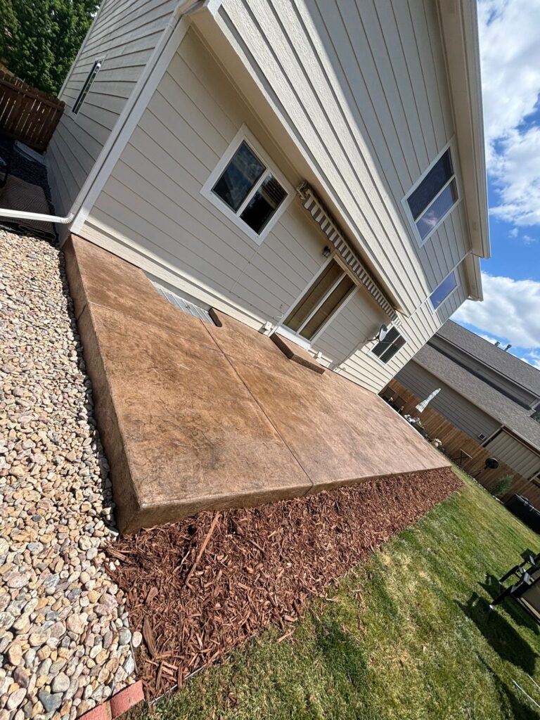 Brand-new light brown stamped concrete patio in Windsor, CO, with a decorative stone-textured finish.